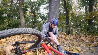 一个年轻人从一辆自行车上摔下来后<strong>坐在公园里</strong>，缓解膝盖的疼痛，在<strong>公园里</strong>骑一辆危险的自行车